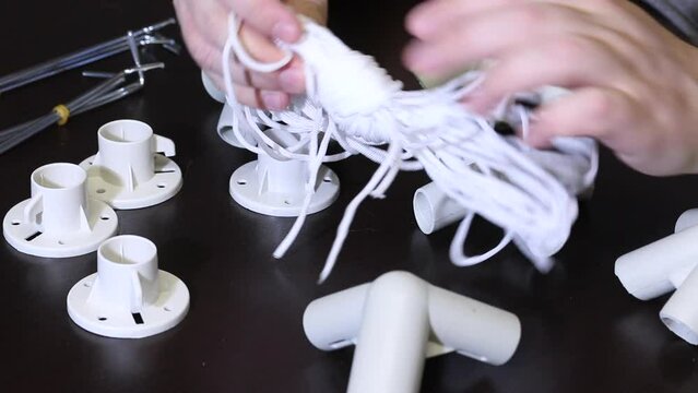 A man demonstrates a set of parts for a garden awning. Examines twine and pegs. Close-up.
