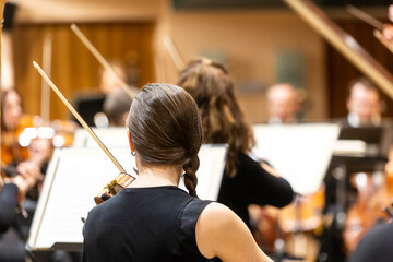 Professional symphonic string orchestra performing on stage and playing a classical music concert, violinist in a foreground - obrazy, fototapety, plakaty