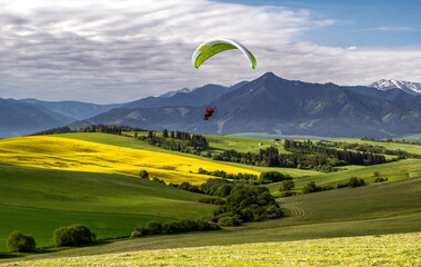Motor paragliding over green agriculture fields and mountains in beautiful country