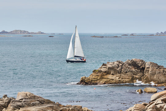 Isles of Scilly, United Kingdom -  sailboat sailing between rocks. rocks in the distance