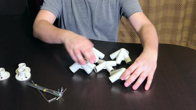 A man demonstrates a set of parts for a garden awning. Looking at adapters. Medium plan.