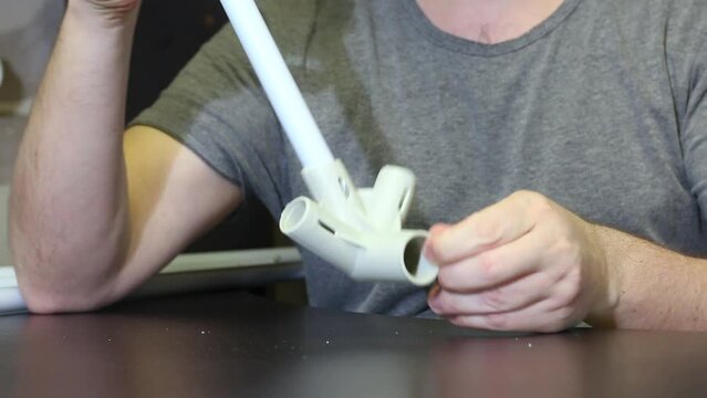 A man demonstrates parts for a garden awning. Connects tubes and adapters. Close-up.