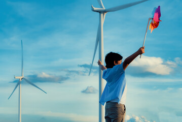 Fototapeta Progressive young asian boy playing with wind pinwheel toy in the wind turbine farm, green field over the hill. Green energy from renewable electric wind generator. Windmill in the countryside concept obraz