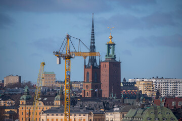 Fototapeta na wymiar A crane, the tower of the church Riddarholms Kyrkan and the Town City Hall, roofs and facades in the old town Gamla Stan, a sunny spring day in Stockholm