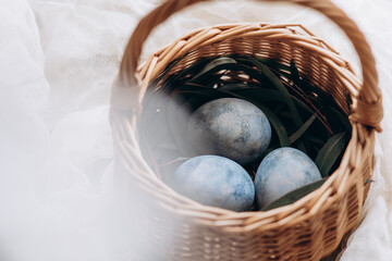 Easter eggs pastel colored in a small wicker basket on light background. Minimal Easter celebration concept, dyed chicken eggs © Ananass