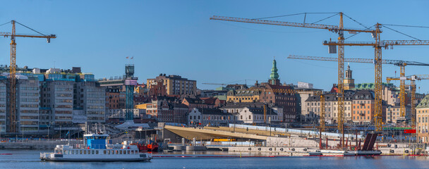 The new sluice construction site, the golden bridge cranes and harbor commuting ferry at hen old town Gamla Stan, a sunny spring day in Stockholm