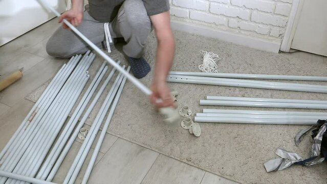 A man is putting together a garden tent. Connects tubes and adapters. Parts for assembly are laid out on the floor