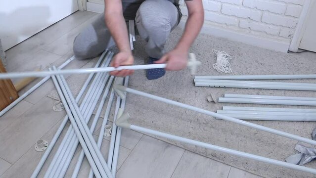 A man is putting together a garden tent. Parts for assembly are laid out on the floor. Connects tubes and adapters.
