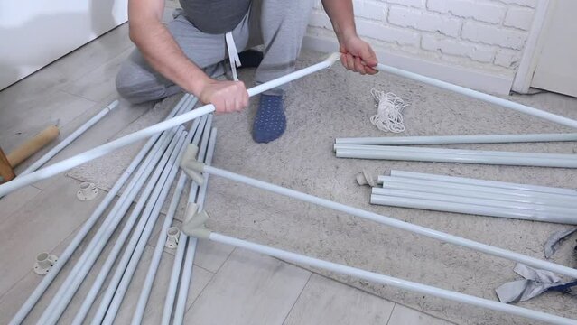 A man is putting together a garden tent. Parts for assembly are laid out on the floor. Connects tubes and adapters
