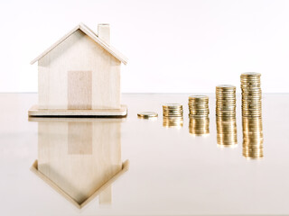 Pile of coins with a wooden house in the background. Concept of purchase expense, rent and mortgage.