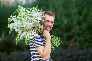 man holding a bunch of white flowers on the background of green garden, looking at camera, summer, spring concept. High quality photo