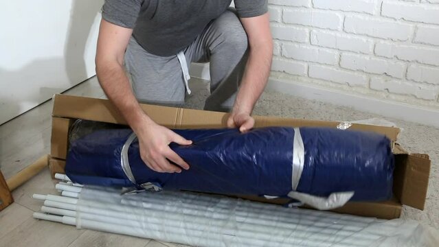 A man unpacks a parcel in a cardboard box. He takes out the construction details for the awning from the box. Garden tent in the package.
