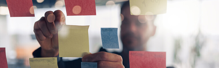 Close up of businessman is glues sticky notes on motivation board in modern office