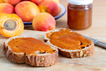 Apricot jam on brown bread slices with half and whole apricots and a jar of jam around.