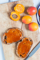 Apricot jam on brown bread slices in top view with half and whole apricots around.