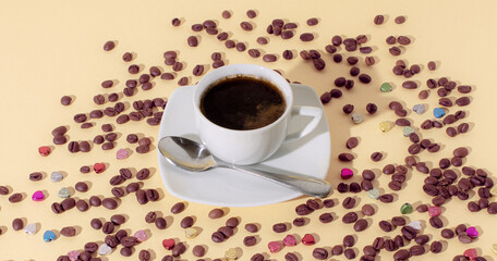 Cup of black coffee with spoon, tiny hearts and coffee beans on yellow background. Minimal horizontal composition, coffee lovers concept