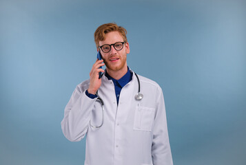 handsome young man doctor isolated on blue background talking on smartphone, smiling positively. Using mobile phone.