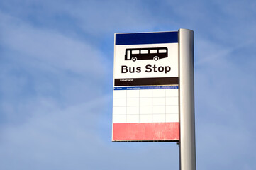 Bus stop sign on post against blue sky