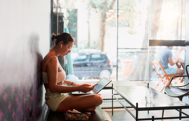 young brazilian digital nomad woman sitting in a hostel working on her laptop and cell phone...