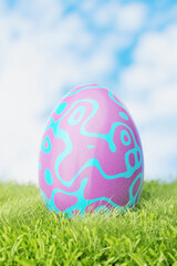 Easter egg in the grass in the meadow. Pink Easter egg in blue patterns. 3d render.
