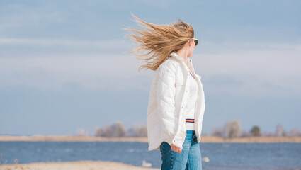 Woman in white jacket, sunglasses and blue jeans at the beach, new collection, fashionable trend