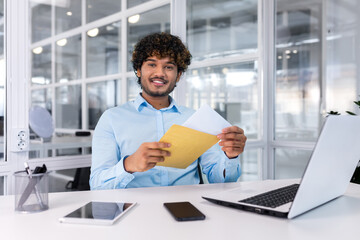 Portrait of a happy Hindu programmer inside the office, a businessman holds an envelope with a good...