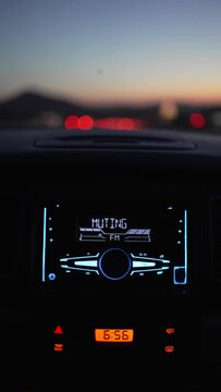 vertical video inside the car, in focus the radio buttons in mutting, in the background motorway lights out of focus, sunset at dusk.