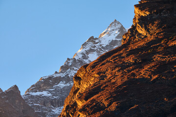 Alpenglow shines on rocky cliffs and a snowy mountain peak
