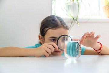 The child examines the water under a magnifying glass. Selective focus.