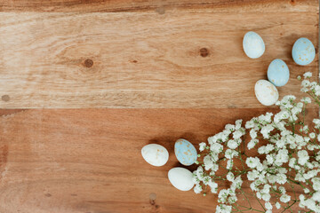 Dyed eggs and white small flowers lie on wooden brown table. Space for text. Mock up. Wooden background with blue and white eggs and white flowers for easter. 