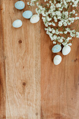 Fototapeta na wymiar Dyed eggs and white small flowers lie on wooden brown table. Space for text. Mock up. Wooden background with blue and white eggs and white flowers for easter. 