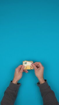 Vid&eacute;o verticale d'une personne qui manipule des billets de banque en euros sur un fond bleu