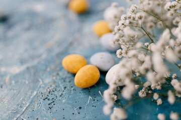 Blue, yellow, white eggs and white small flowers lie on a beautiful blue and turquoise picturesque background. Spring Background for Easter
