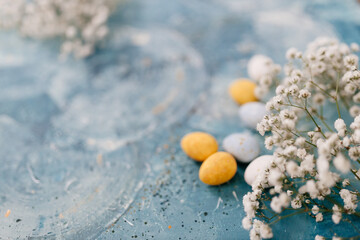 Blue, yellow, white eggs and white small flowers lie on a beautiful blue and turquoise picturesque background. Spring Background for Easter
