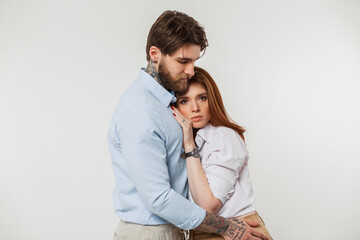 Stylish beautiful fashionable couple hugging in the studio against a white background. Handsome hipster man embraces redheaded girl in fashionable elegant clothes