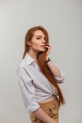 Beautiful sexy redhead woman with long red hair in a fashionable white shirt on a white background in the studio