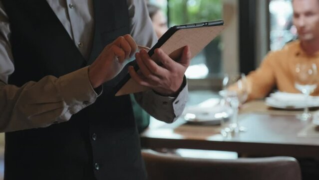 Cropped shot of waiter in classic uniform using digital tablet while taking order in restaurant