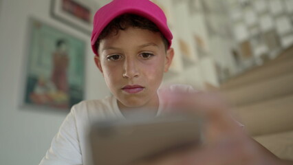 Portrait of young boy using phone at home. Close up preteen child face looking at smartphone device browsing social media online
