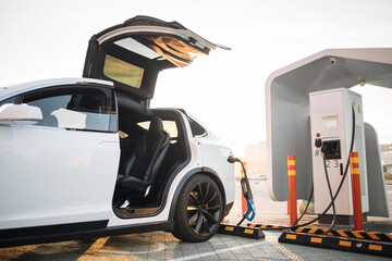 Modern luxury electric car charging at outdoors EV station with blurred urban area on background....
