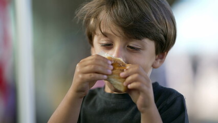 Portrait of child eating piece of bread croissant. Close up face of one small boy kid eating carb food