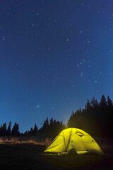 Luminous tourist tent under the starry sky. Tourist tent at night in the forest. Starry sky above the tent.