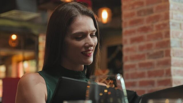 Young beautiful woman reading menu and choosing dishes while eating out in restaurant