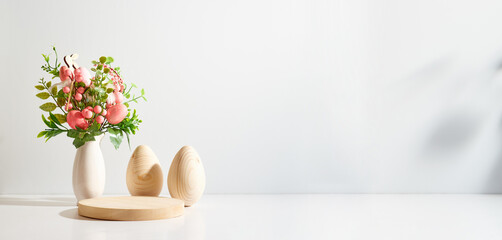 Empty round wooden podium for product presentation. Spring flowers in a vase and easter eggs on a light background.
