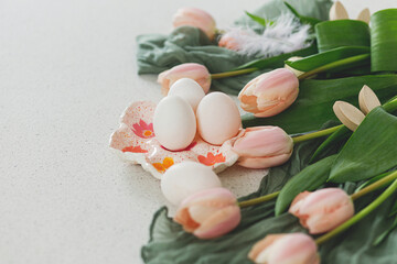 Beautiful tulips, natural eggs and bunny decoration on modern table. Stylish easter still life with copy space. Happy Easter! Handmade egg holder, pink tulips and wooden bunny ears