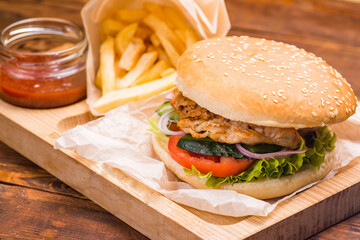 Burger with cutlet in a white bun on the background of french fries and tomato sauce