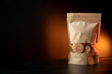 Oat and corn flakes cookies. Healthy natural food. Yellow paper kraft bag. Black background with orange light glow.