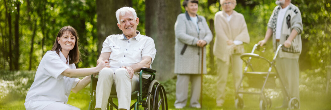 Mature Caregiver And Elder Man On The Wheelchair