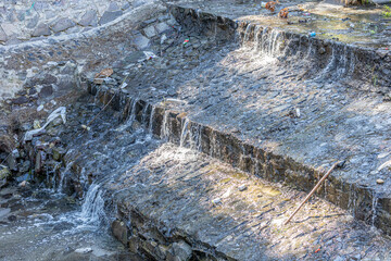 Open sewage stone channel with a spillway with garbage on the accumulated surface and little...