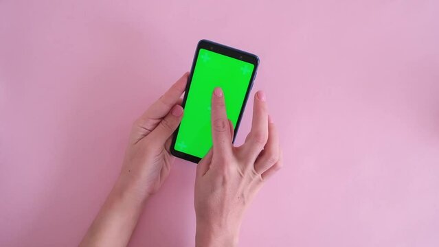 Close-up of female hands scroll phone with green screen on pink background