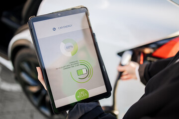 Close up of businesswoman in suit using digital tablet during electric automobile charging session...